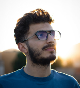man in blue tshirt wearing sqaure framed glasses and posing outside in the evening